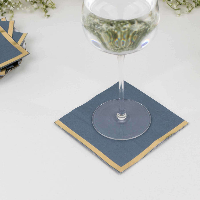Blue and gold paper cocktail napkin under a glass of water.
