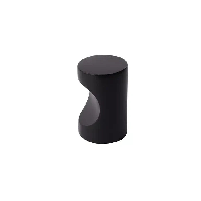 A small, cylindrical black metal object with a flat top and a curved notch on one side, resembling a modern Taymor Industries cabinet knob or drawer pull, is shown against a plain white background.